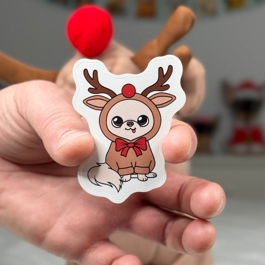 Hand holding a cartoon dog in a reindeer costume sticker with a blurred background