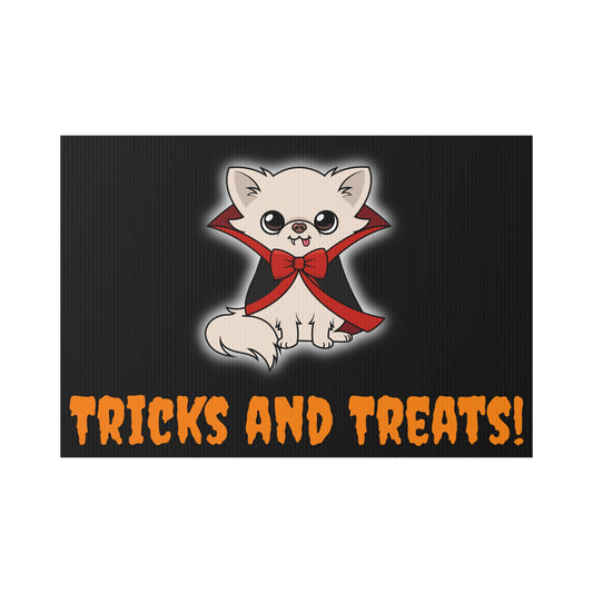 Rectangular black lawn sign with a cute cream chihuahua sitting in a black cape with red lining and a red bow, small fangs and tongue showing, with orange text at the bottom that reads “TRICKS AND TREATS!”.