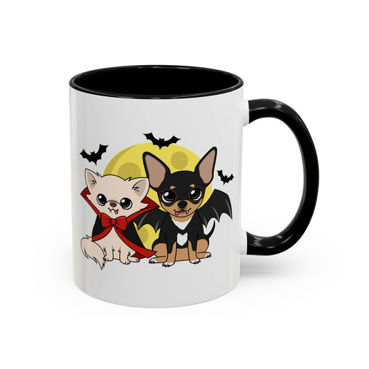 White ceramic mug with a black handle and interior, featuring a cute illustration of two chihuahuas in front of a soft yellow moon, one cream dog in a red cape and bow and one black-and-tan dog with small bat wings, surrounded by flying bats.