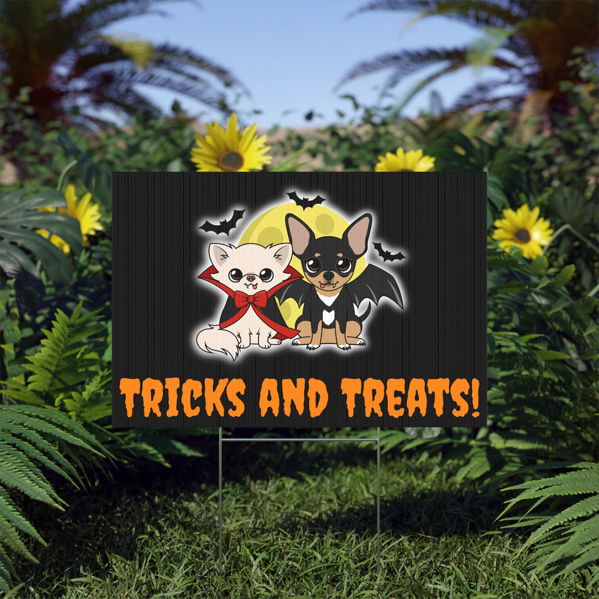Halloween yard sign showing two cartoon chihuahuas in front of a yellow moon, one in a red-lined vampire cape and bow and the other with bat wings, with flying bats above and the text “TRICKS AND TREATS!” in orange at the bottom.