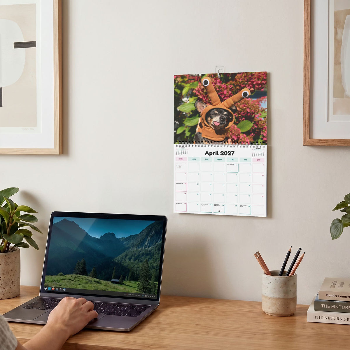 2027 wall calendar displayed above a desk, open to April and showing Cedric and Maya.