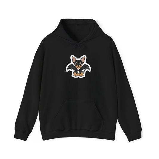 Front view of a black hoodie featuring a centered cartoon black-and-tan chihuahua with bat wings, a small fang, and a soft white outline around the character.