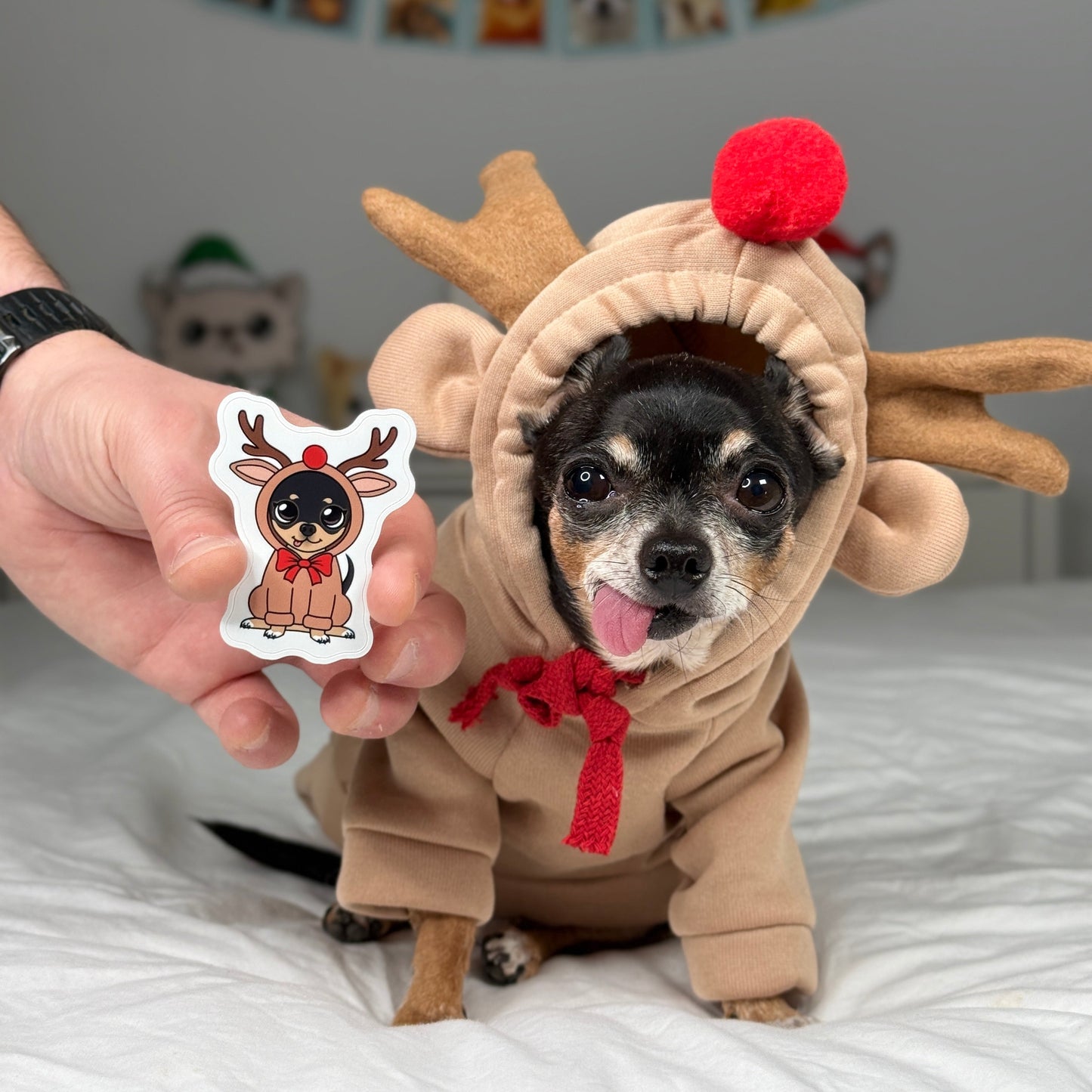 Dog in a reindeer costume holding a sticker of a dog in a similar costume, with a festive background.