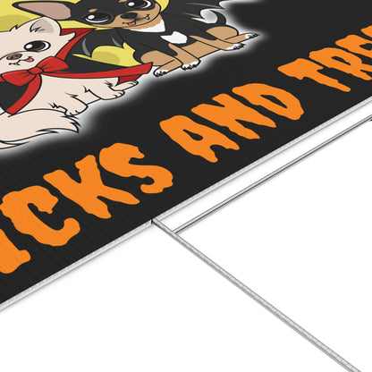 Close-up of a black Halloween lawn sign showing two cartoon Chihuahuas in front of a yellow moon—one cream dog in a red-lined cape and bow and one black-and-tan dog with bat wings—above large orange spooky lettering, with the metal H-stake visible beneath the corrugated edge.